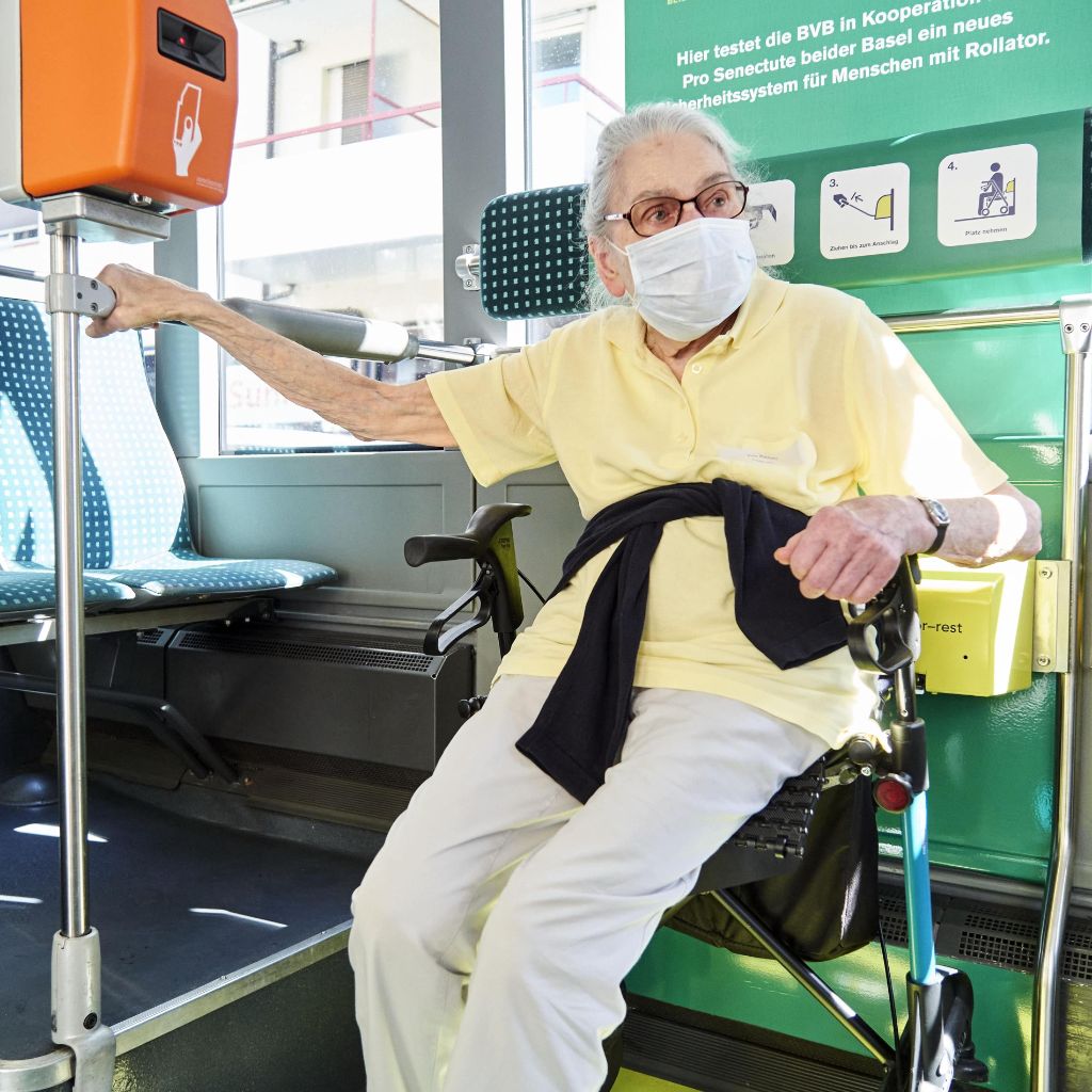 Seniorin sitzt in einem Bus auf ihrem Rollator.