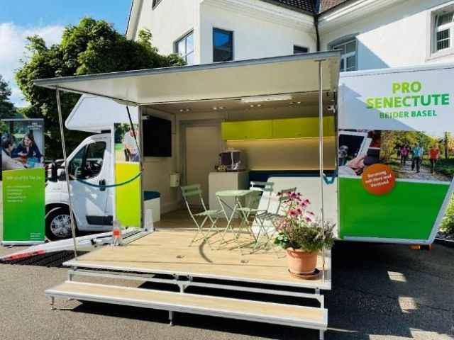 Infobus ist im Einsatz und hat einen Tisch sowie mehrere Stühle bereitgestellt.