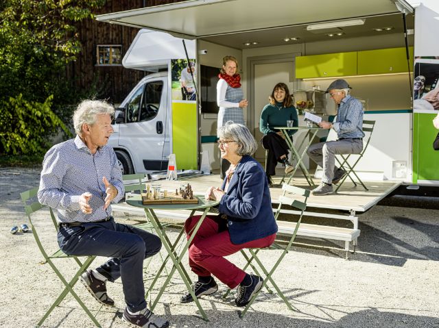 Eine Gruppe von Menschen treffen sich beim Infobus und reden miteinander oder spielen Schach.