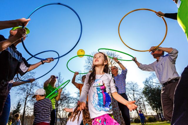 Personen unterschiedlichen Alters spielen im Freien mit Bällen und Hula-Hoop-Reifen.