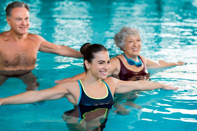 Personen unterschiedlichen Alters nehmen an einem Wassergymnastik-Kurs in einem Hallenbad teil.