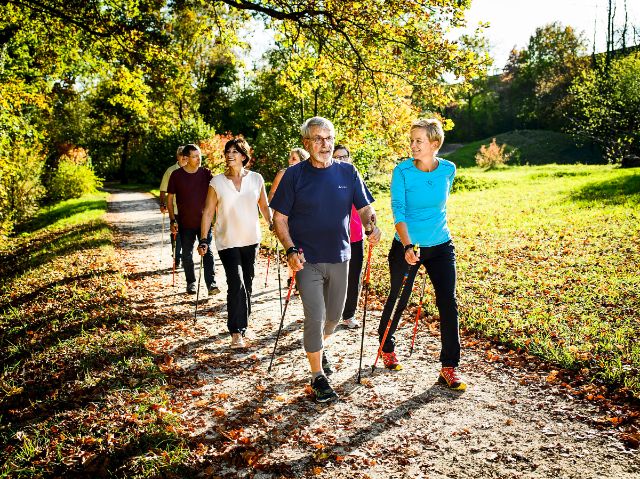 Eine Gruppe älterer Menschen wird beim Nordic Walking von einer Kursleiterin geleitet.