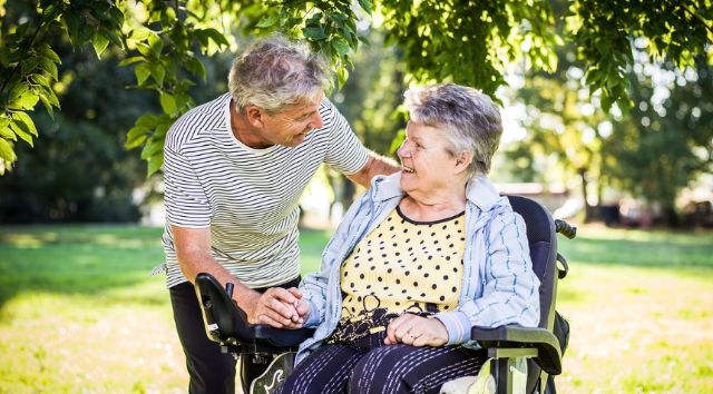 Eine Seniorin im Rollstuhl lacht und unterhält sich mit einem ebenfalls lachenden Angehörigen.