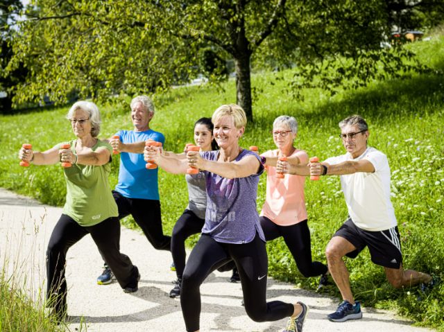 Eine geschlechter- und altersgemischte Gruppe treibt in der Natur mithilfe von Gewichten Sport.